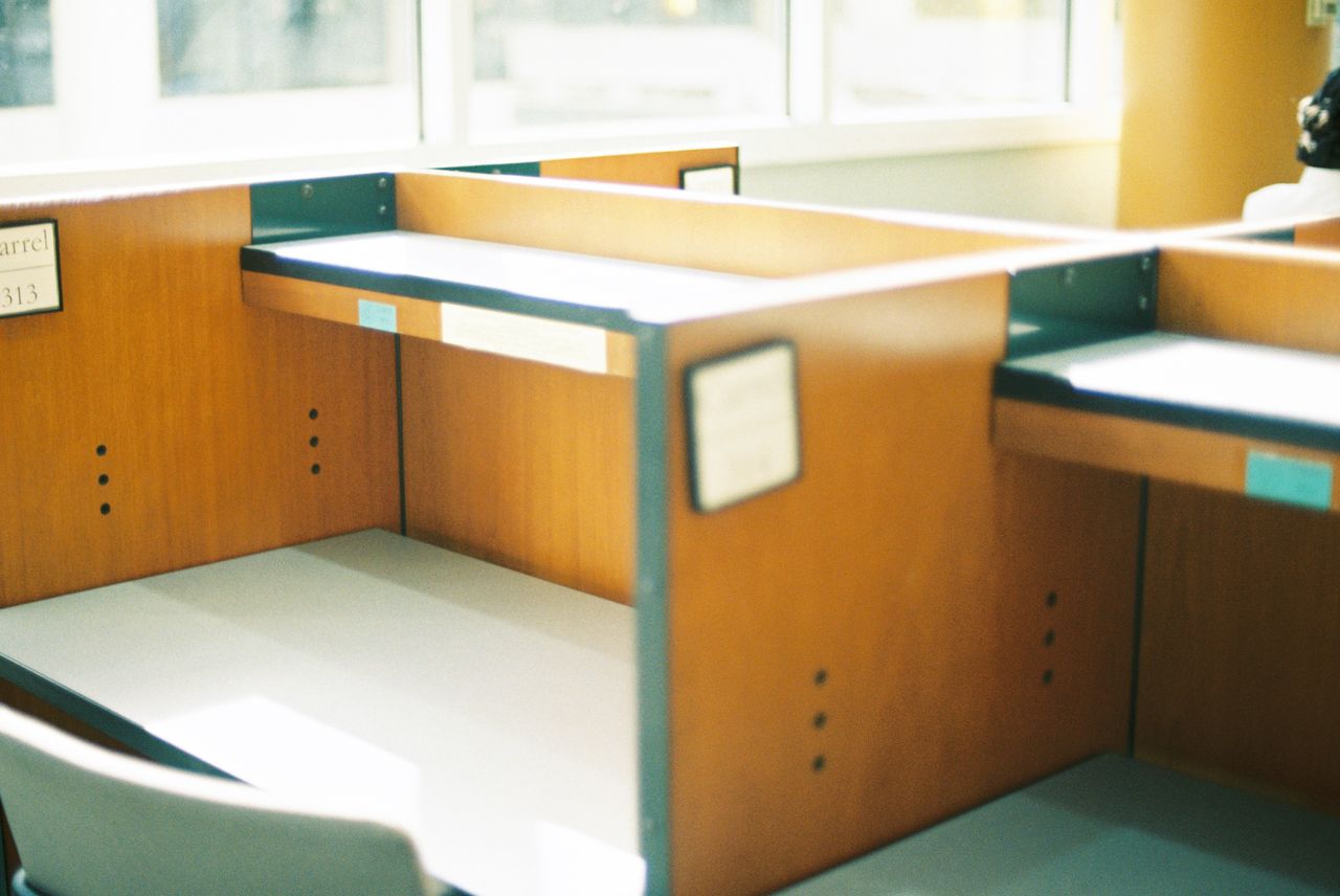 Hello world! Empty wooden cubicles in a sunlit office space, offering a modern professional ambience.