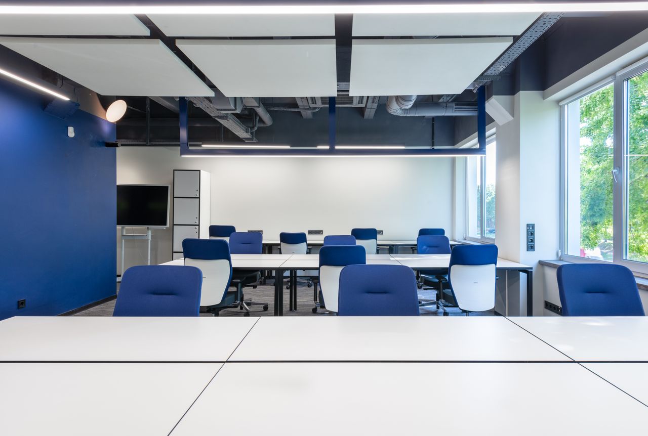 services-01 Various white desks with blue chairs placed in modern spacious workspace with big window and monitor in contemporary business center